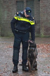 Caïro zit naast zijn baasje Patrick die een politiepak aan heeft